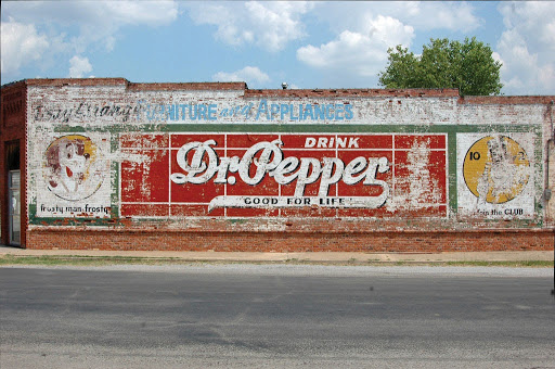 Side view of a brick building displaying a faded Dr. Pepper mural.