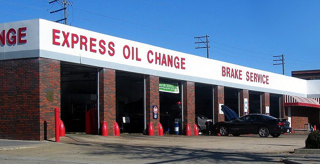 Outside view of Express Oil Change business. Brick building with a car outside being worked on. The sky above is bright blue.