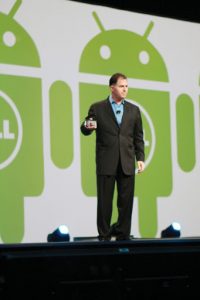 Michael Dell giving a speech wearing a black suit standing on a stage in front of green Dell robot icons.
