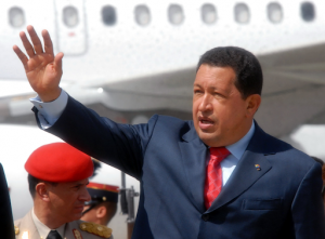 Hugo Chavez outside in front of a plane in Guatemala. He is wearing a suit with a red tie and has his hand up waving to someone.