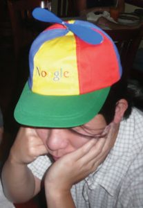 A young man wearing a primary colored helicopter hat with 'Noogle' embroidered on the front.