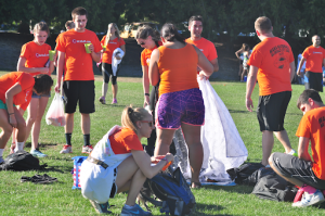 Co-ed adult kickball team wearing matching orange shirts and cleaning up the field.