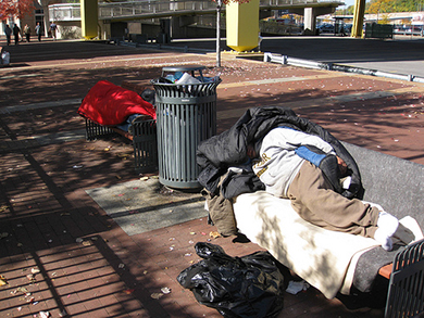Photo of two homeless people asleep on public city benches