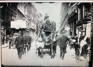 a historical photo in which police officers escort a delivery truck down a city road 
