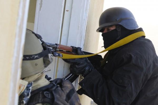 An armored police officer is shown in a doorway holding and pointing his gun.
