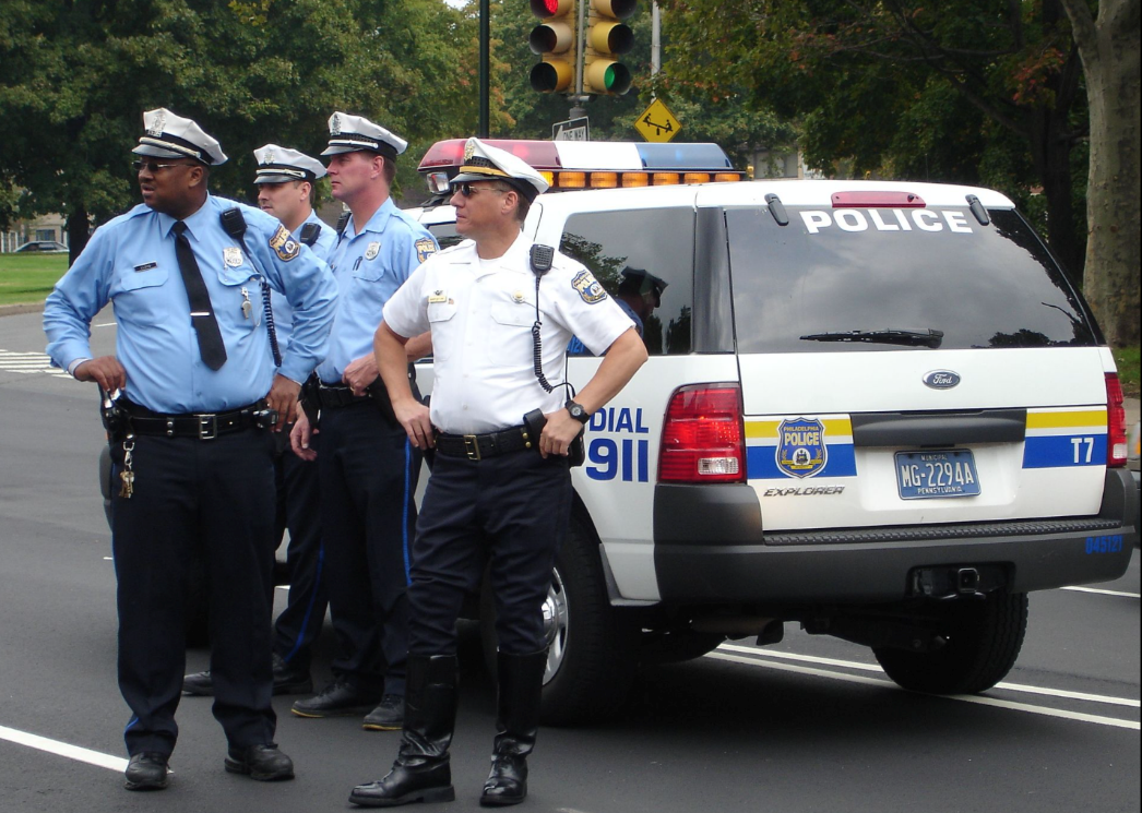 police officers observing a scene while standing in front of a police car 