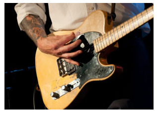 Hombre rasgueando una guitarra eléctrica durante un concierto de rock.