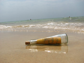 Photo of a glass bottle with a message in it, lying in the sand at the beach.