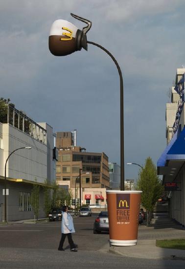 A man walks by an odd lamppost. The bulb of the light looks like a McDonald's coffeepot, while the base of the lamp looks like a McDonald's coffee cup. The pole of the lamppost looks like coffee being poured from the coffeepot into the cup.