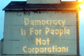 Photo of an old building with the words "Democracy Is For People, Not Corporations" painted in yellow.