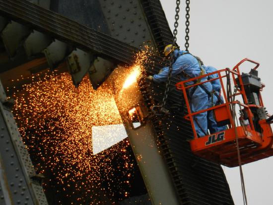 Photo of a construction worker on the side of a building, welding. Bright sparks fly.