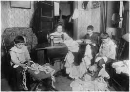 Foto en blanco y negro que muestra a una familia de cuatro personas sentada en un salón o sala cosiendo ropa de muñeca.