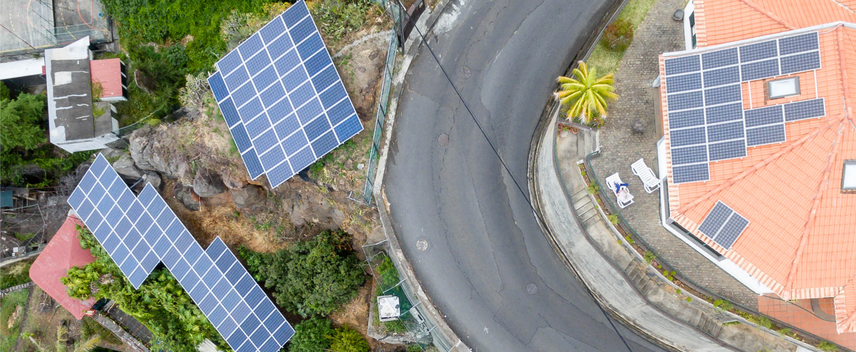 Une photographie aérienne montre des maisons sur une colline tropicale avec des panneaux solaires sur leurs toits.