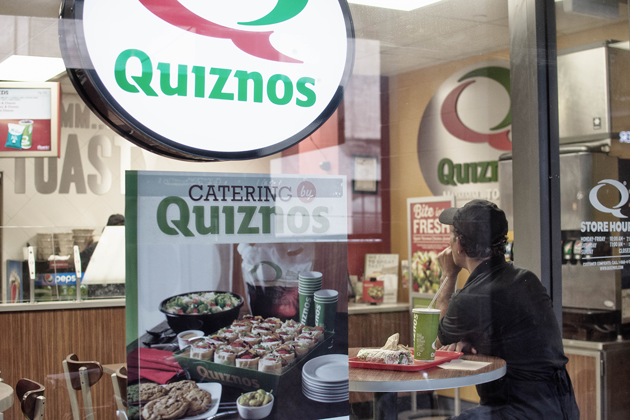 A photograph shows inside of a small Quiznos restaurant.