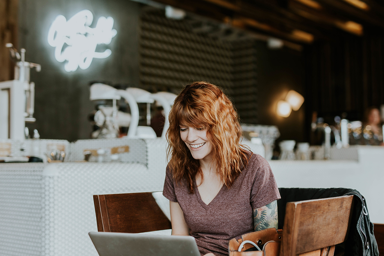 Uma fotografia mostra uma mulher em um laptop enquanto ela está sentada em uma cafeteria.