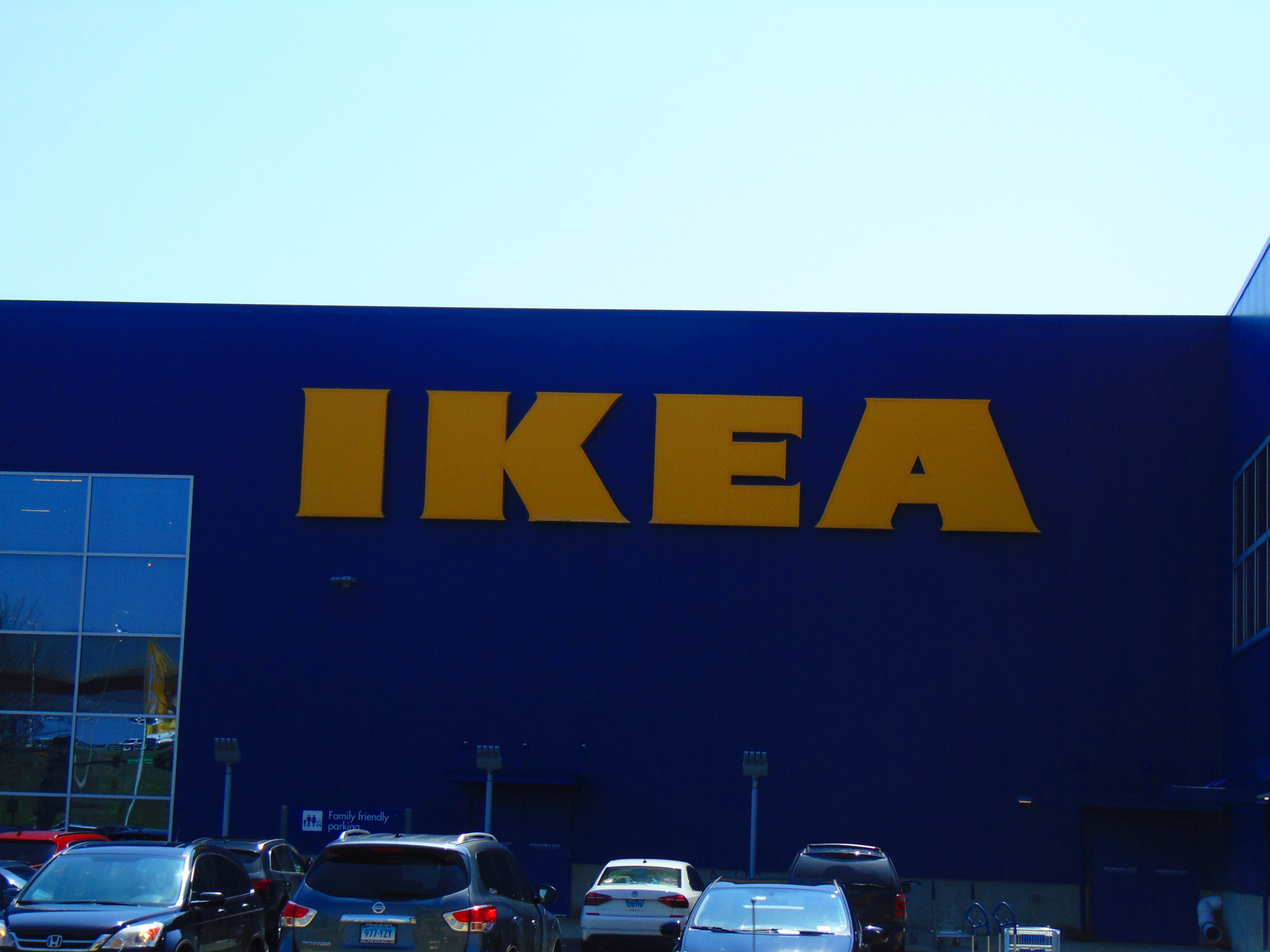 Une photo montre un grand bâtiment Ikea avec des voitures garées à côté.