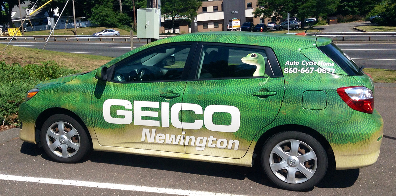 Une photographie montre une voiture dont la peinture ressemble à la peau d'un gecko. De grandes lettres indiquent Geico, et il y a un autocollant représentant le gecko Geico sur la fenêtre.