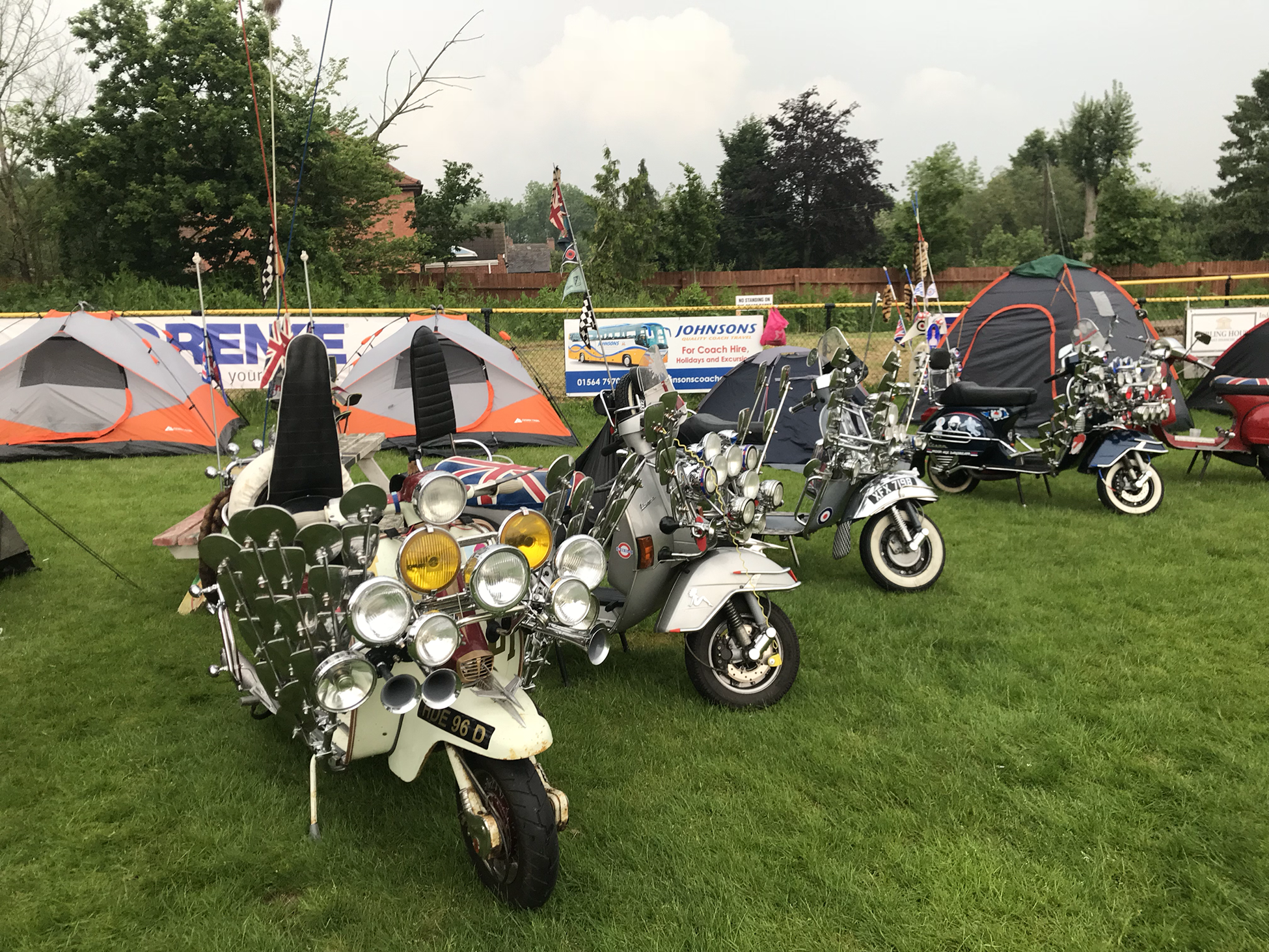一张照片显示定制的 Vespa 踏板车停在草地上，背景是帐篷。