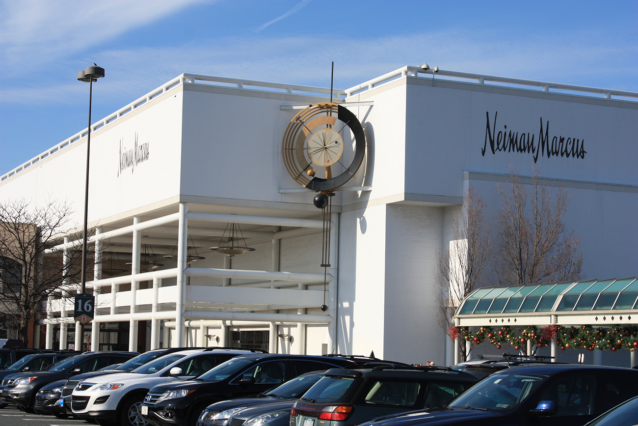 Une photographie montre l'extérieur d'un magasin Neiman Marcus. C'est un grand bâtiment avec une grande statue d'horloge en métal et une passerelle couverte décorée de décorations de Noël.