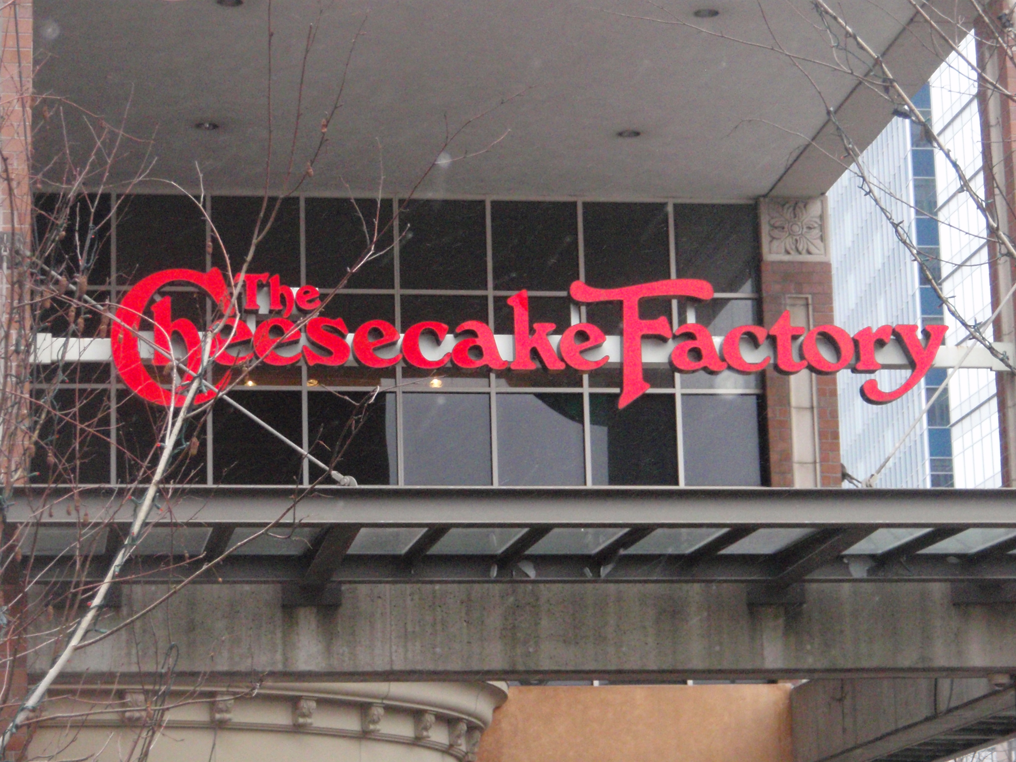 一张照片显示建筑物入口上方悬挂着一个大型芝士蛋糕工厂的标志。