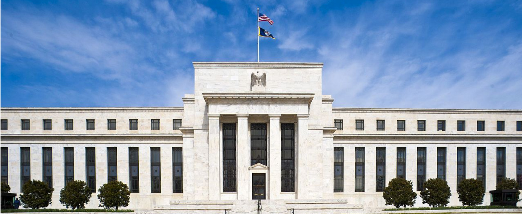 O Edifício do Conselho da Reserva Federal Marriner S. Eccles é exibido. O edifício muito grande, localizado em Washington DC, é construído em mármore branco e tem uma grande entrada.