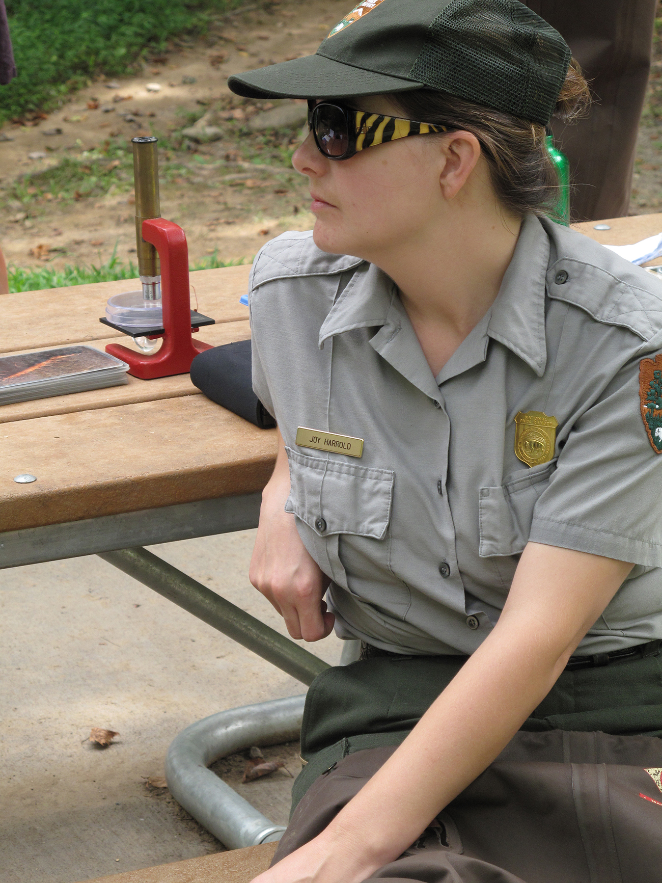 Um guarda florestal, vestindo um uniforme oficial e um distintivo, senta-se em uma mesa de piquenique do lado de fora.