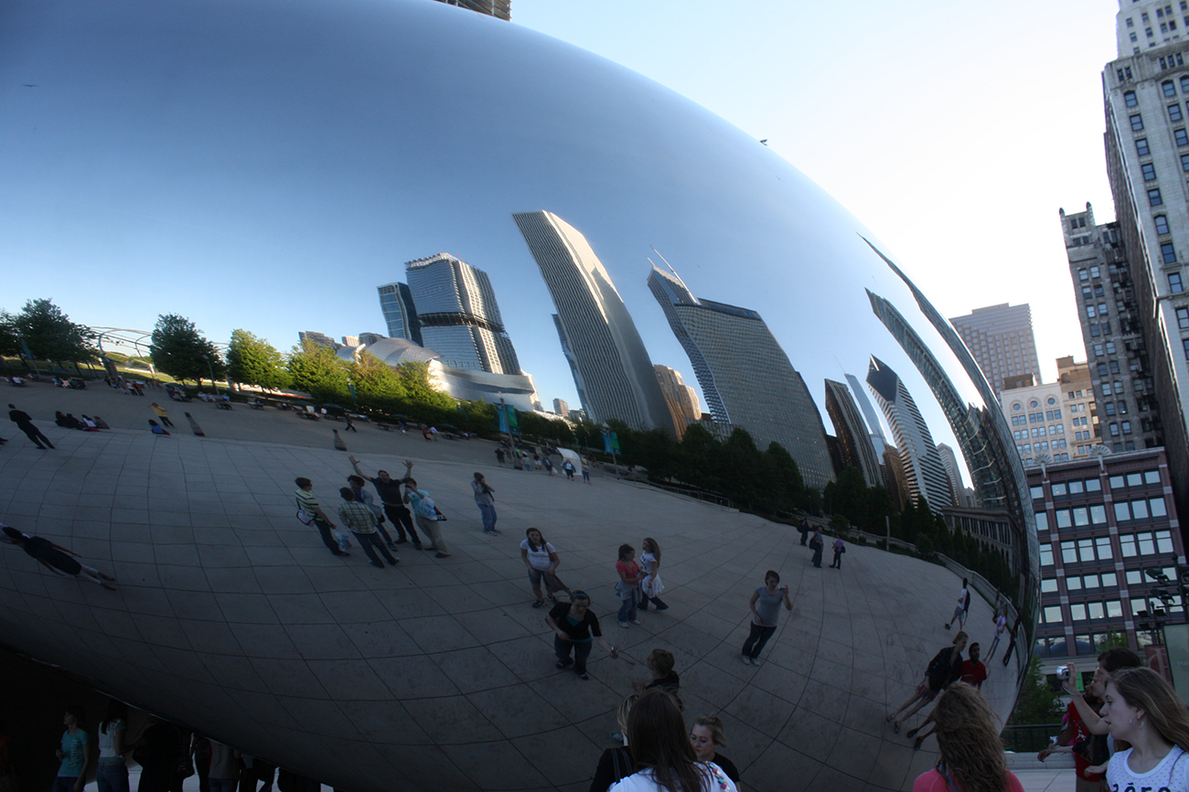 A photo shows the large, extremely smooth and reflective bean shaped sculpture. The city skyline reflects in the bean's surface.