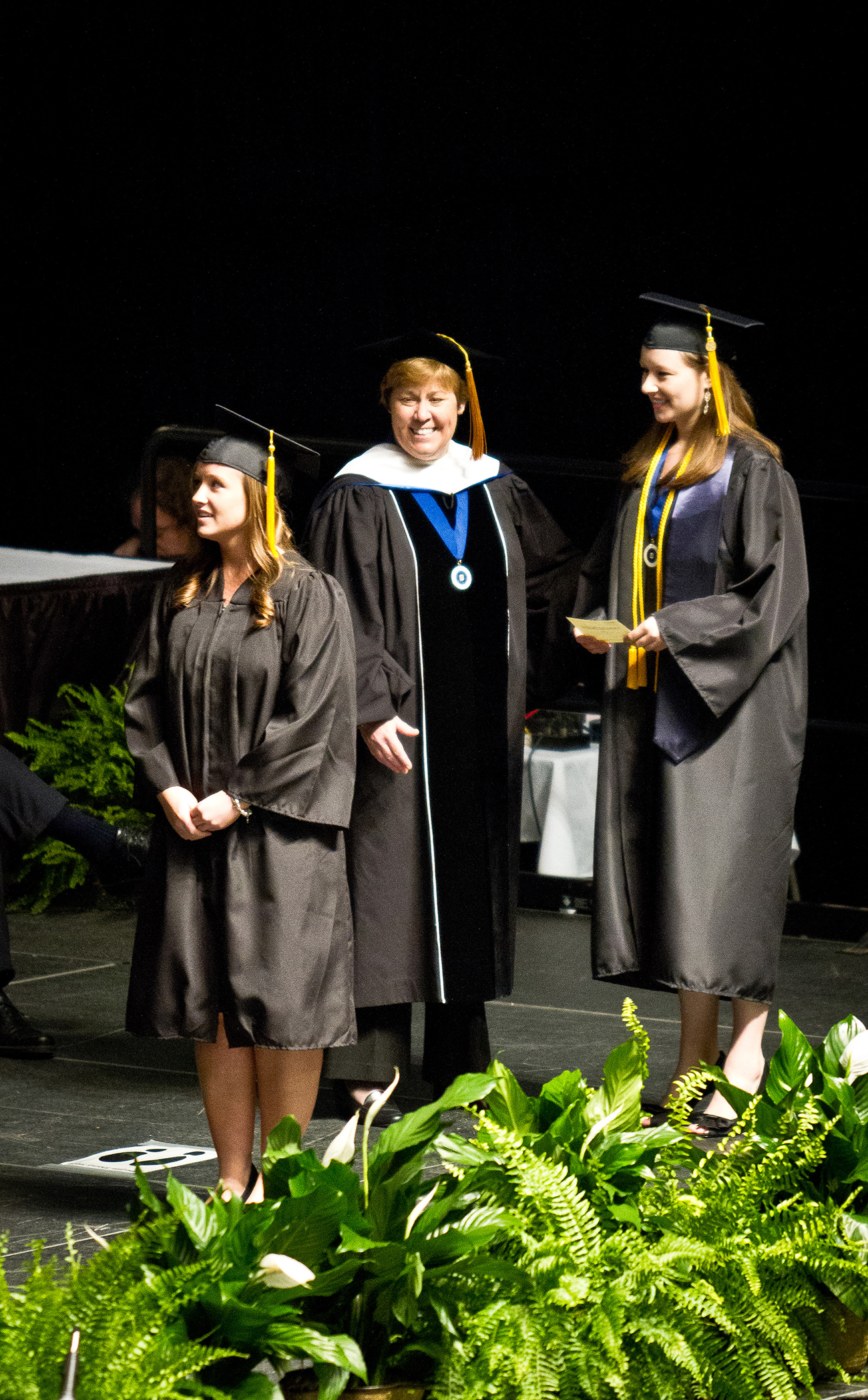 Graduados, vestindo boné e vestido, atravessam um palco para receber seus diplomas.
