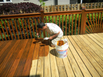 Photo of a man brushing wood stain on a new wooden deck.