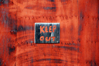 Small black sign with red lettering that reads, "Keep Out." Background is red, too.