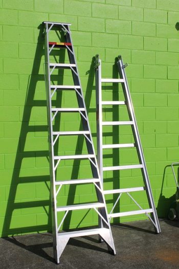 Photo of two ladders leaning against a green wall.