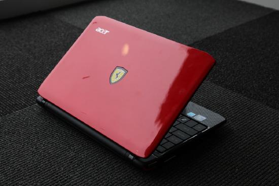 Red Acer Ferrari laptop shown partly open on a grey carpeted surface.