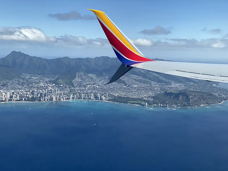 Image of a wing of a Southwest Airline airplane flies over a body of water.