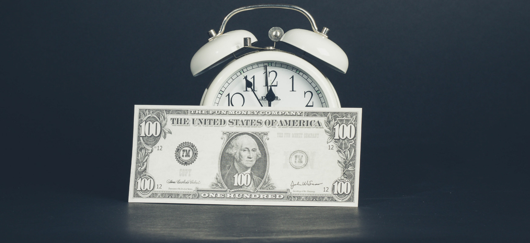 A $100 bill leans against an alarm clock.