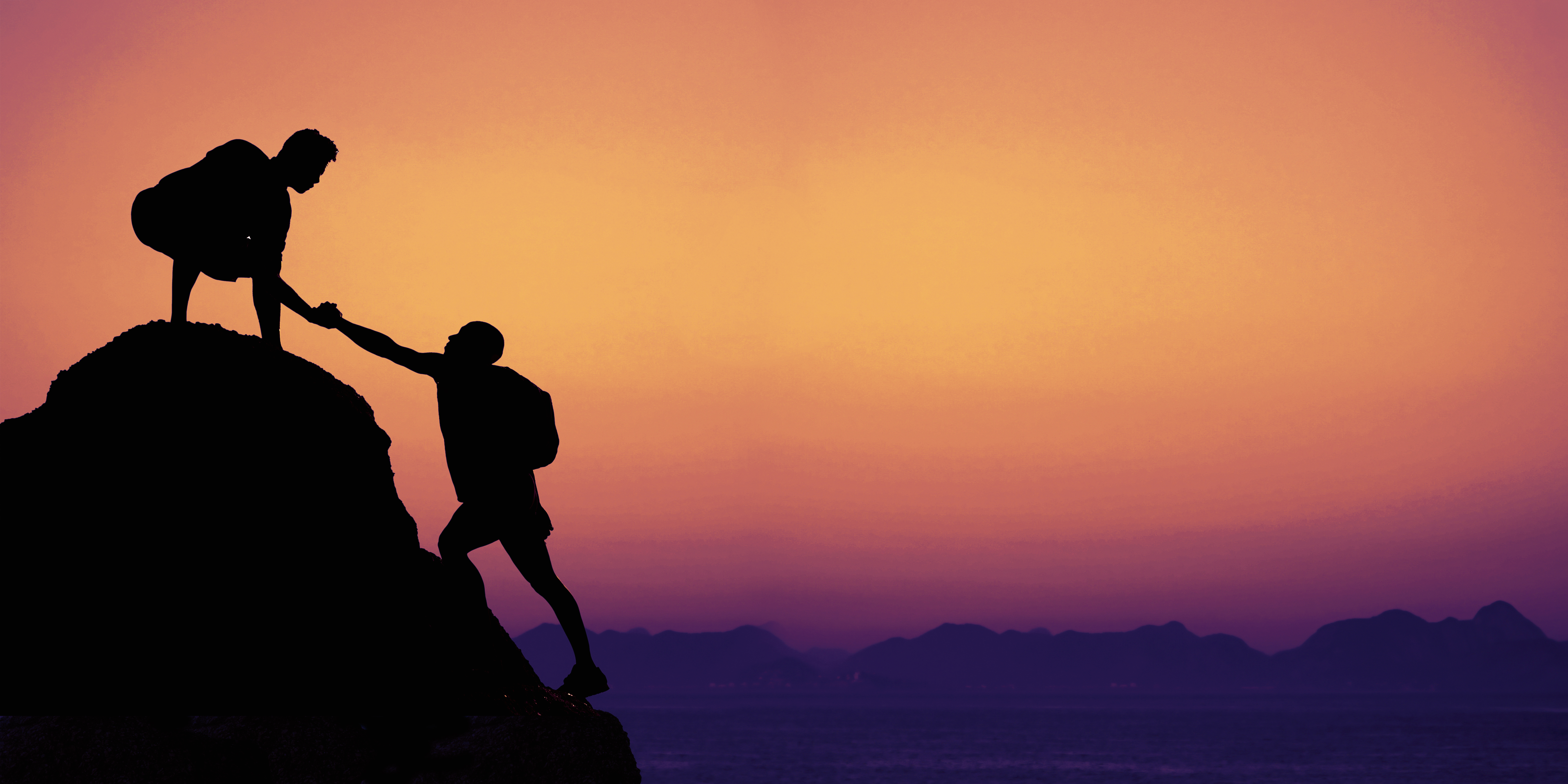 Two silhouetted figures on a rocky ledge, one helping the other climb, against a purple sunset backdrop.