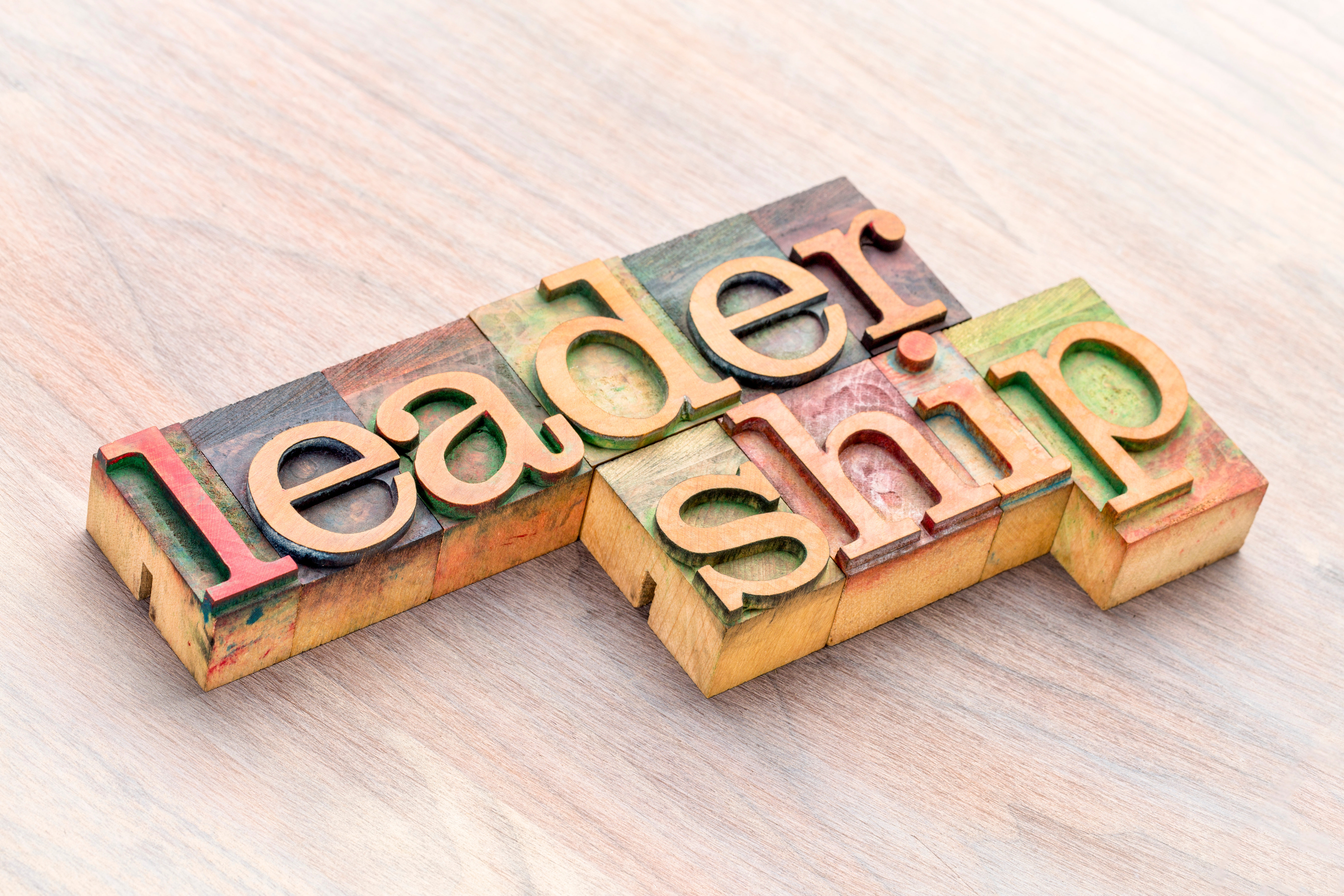 Colorful wooden letters spelling "leadership" on a wooden surface.