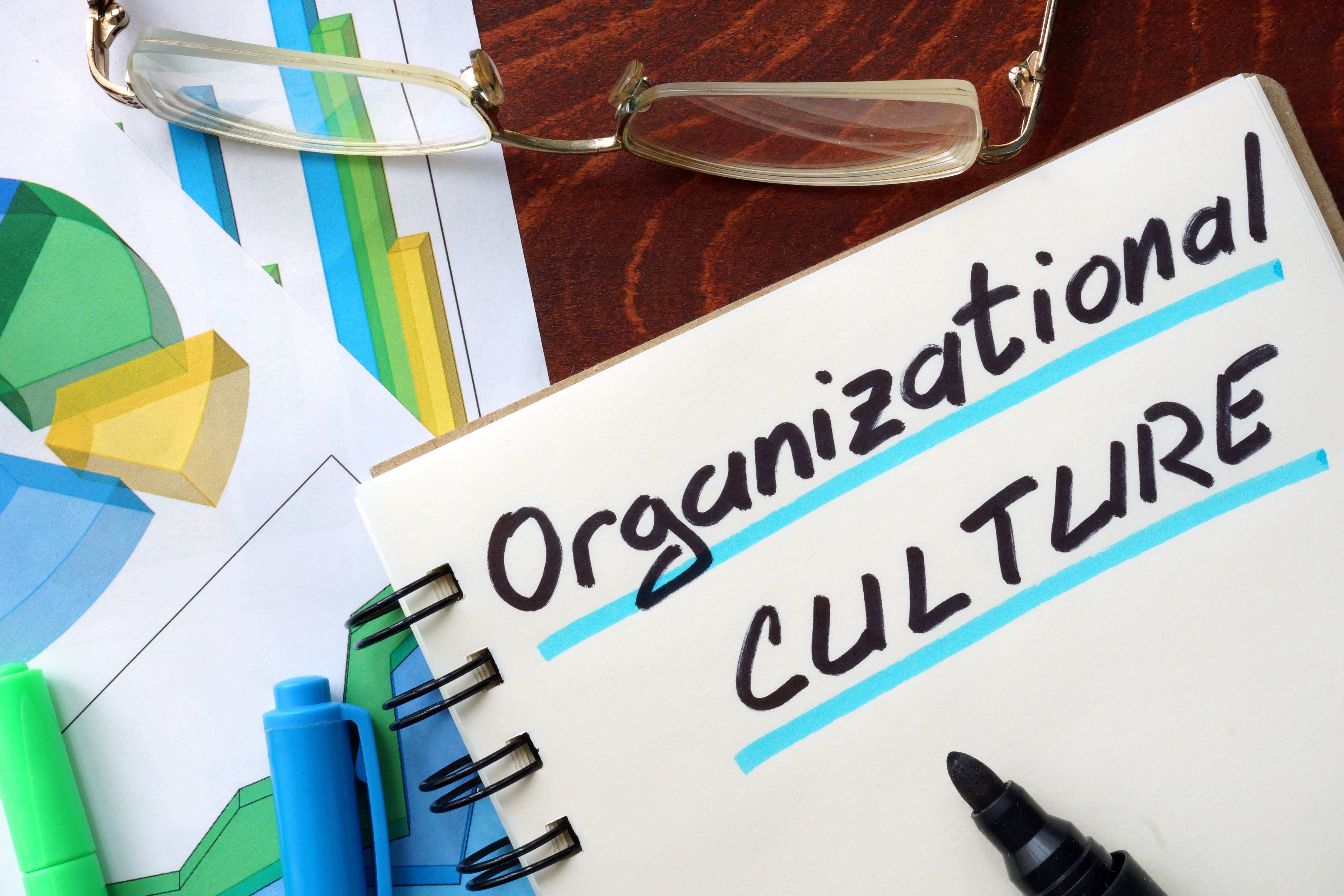 Notebook page with "Organizational CULTURE" written on it, surrounded by glasses, colorful markers, and graphs.