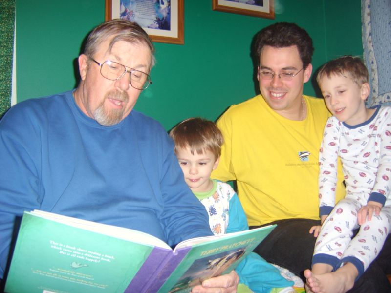 Abuelo lee un libro en voz alta mientras un papá y 2 hijos escuchan