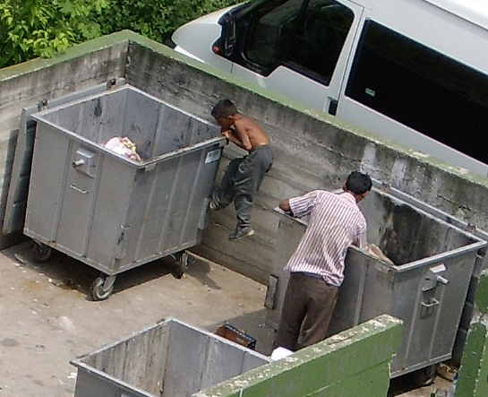 Two people dumpster diving in a parking lot