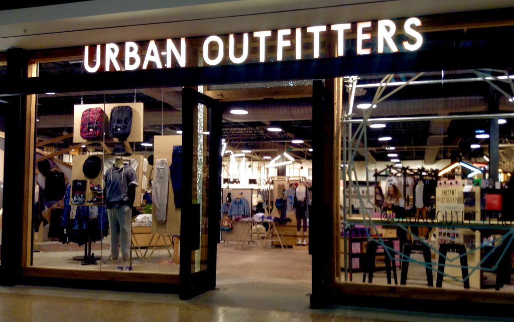 A storefront for Urban Outfitters. Near the front of the store are mannequins wearing the store's clothing. The inside of the store has industrial spotlights, a cement floor, aisles of clothing, and more mannequins."A storefront for Urban Outfitters. Near the front of the store are mannequins wearing the store's clothing. The inside of the store has industrial spotlights, a cement floor, aisles of clothing, and more mannequins.