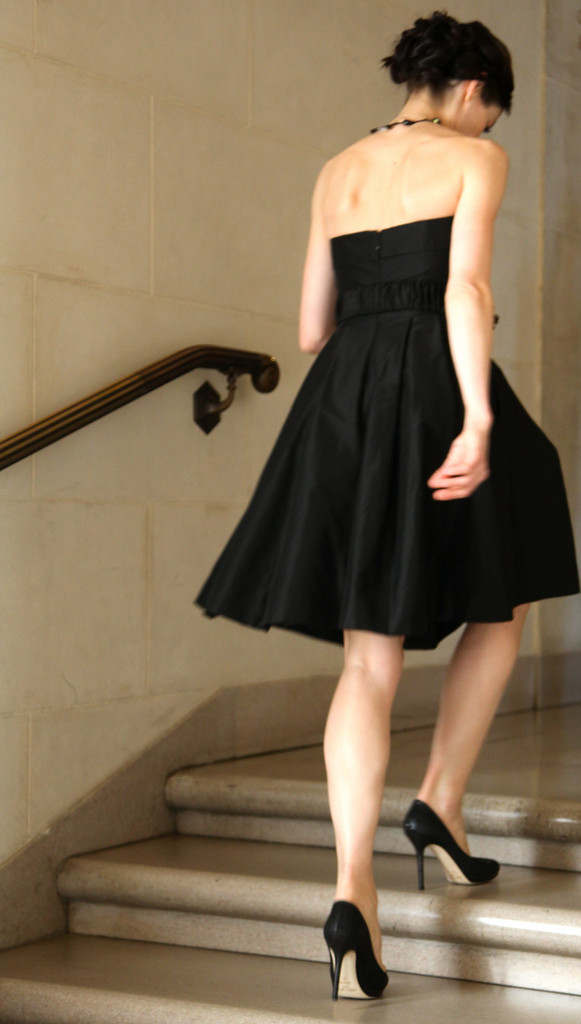 A woman wearing a cocktail dress and heels walking up some steps.
