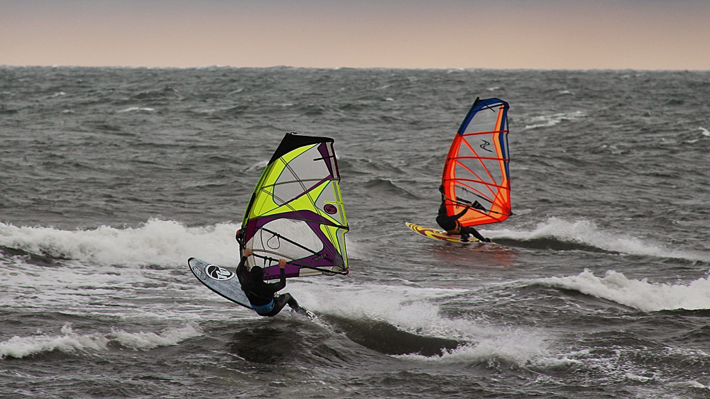 2 windsurfers parallel to each other race across the water. 