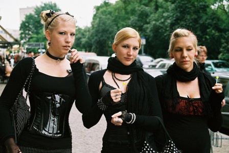 Foto de tres jovencitas vestidas con atuendos góticos caminando afuera en una ciudad.