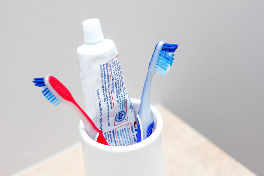 Fotografía de dos cepillos de dientes en una taza blanca con pasta de dientes