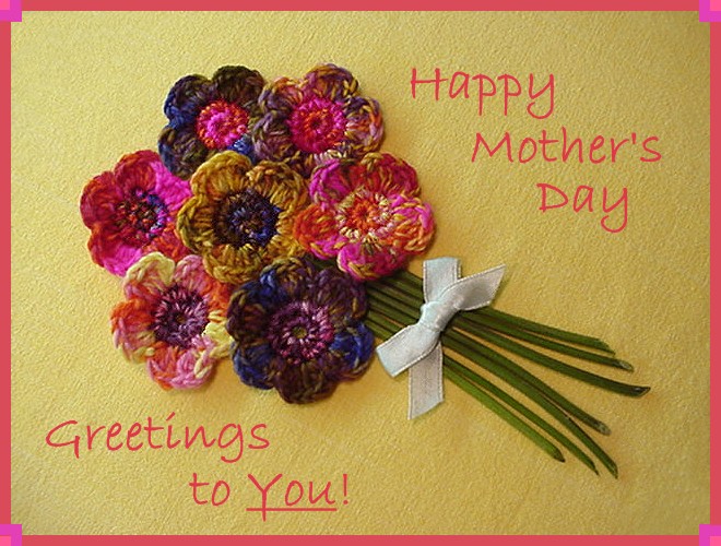 Tarjeta de felicitación que dice: “¡Feliz Día de la Madre Saludos a Ti!” La tarjeta tiene un ramo de flores de punto rosadas y moradas en el centro.