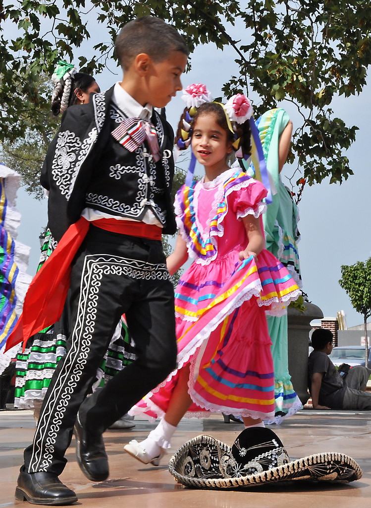 A young boy and girl dressed in fancy traditional clothing dance together at Latino cultural festival.