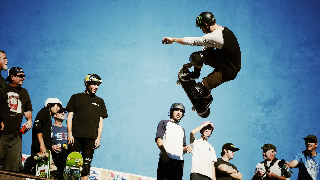 A group of skateboarders watch as another skateboarder performs an aerial stunt.