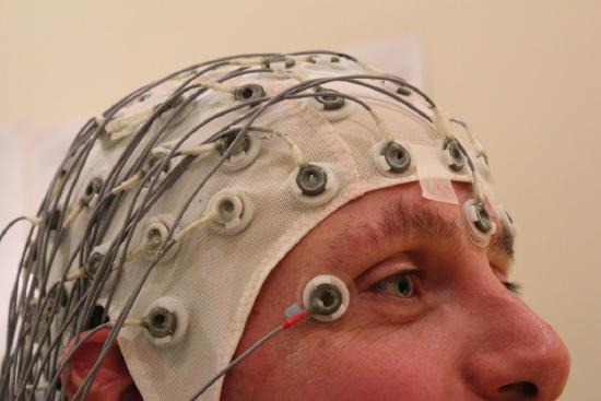 Photo of the upper half of a man's head is shown. He's wearing a mesh fabric cap with multiple electrodes connected to it.
