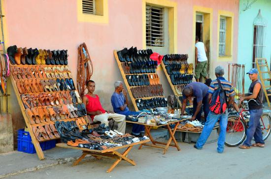 Tables on the street filled with shoes available for sale. A few customers peruse the shoes.
