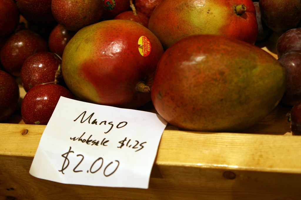 Una canasta de mangos en el supermercado. Un letrero dice mango $2, venta al por mayor $1.25.